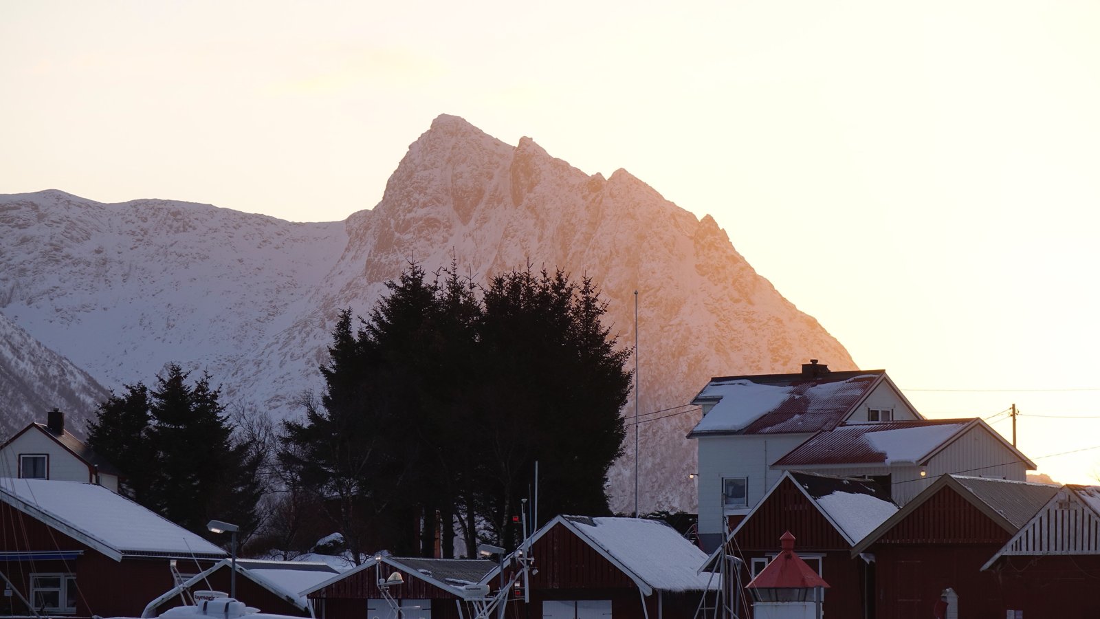 Hus på Meløy i kveldssol med snødekte fjell bak